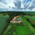 Vista aérea de uma propriedade rural com piscina, áreas verdes e campos ao redor.