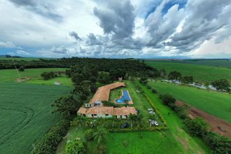 Vista aérea de uma propriedade rural com piscina, áreas verdes e campos ao redor.