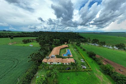 Vista aérea de uma propriedade rural com piscina, áreas verdes e campos ao redor.