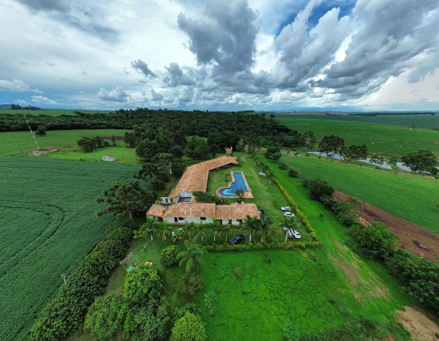 Vista aérea de uma propriedade rural com piscina, áreas verdes e campos ao redor.