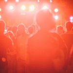 Público reunido diante de um palco iluminado durante um festival de música ao ar livre