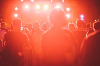 Público reunido diante de um palco iluminado durante um festival de música ao ar livre