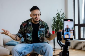Homem grava um vídeo em casa usando um smartphone apoiado em um tripé.