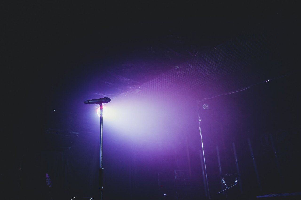 Microfone sobre um palco com iluminação roxa, preparado para um show musical.
