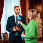 Jornalista entrevista um profissional em um ambiente formal.