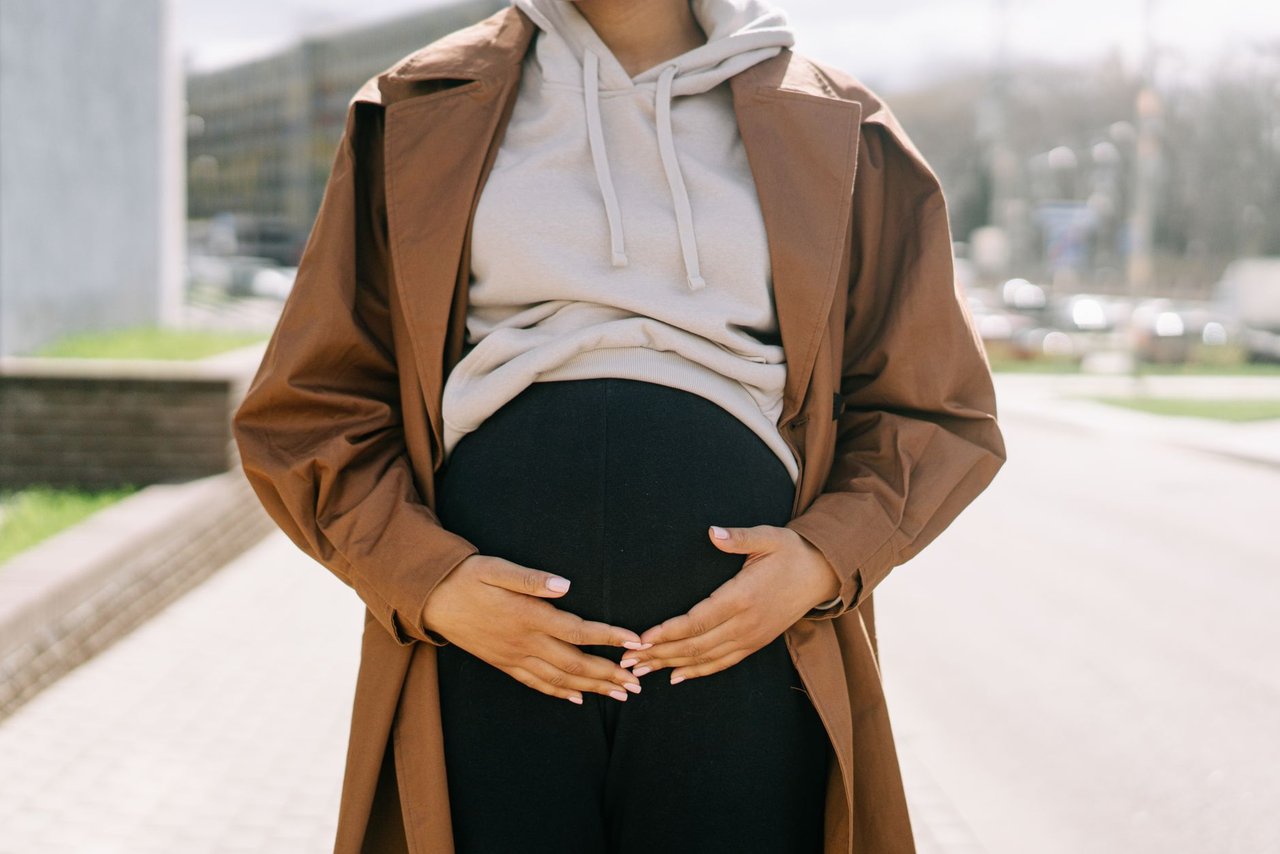 Mulher grávida em ambiente urbano, com as mãos sobre a barriga.
